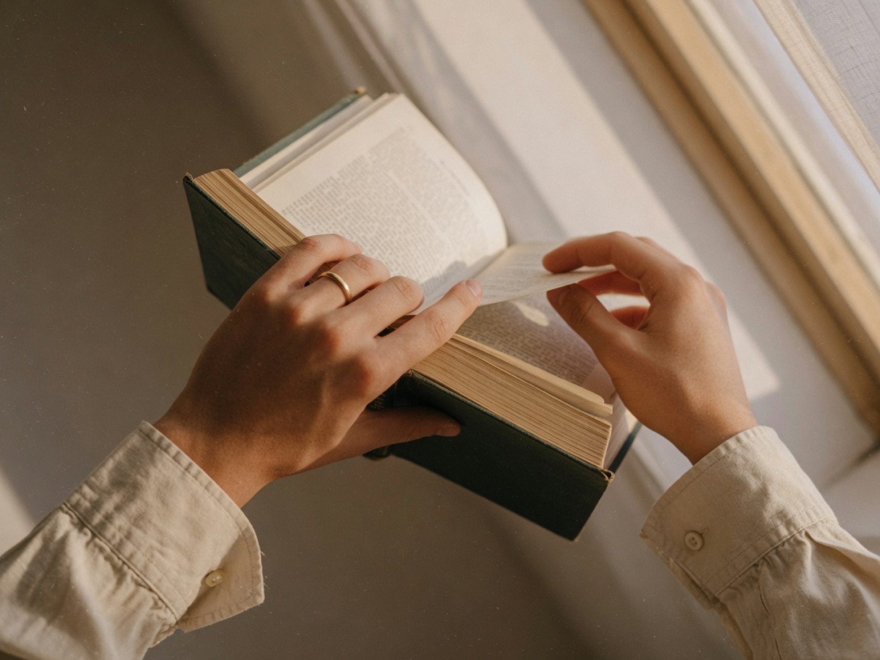 Hands turning the pages of a hardcover book in window light