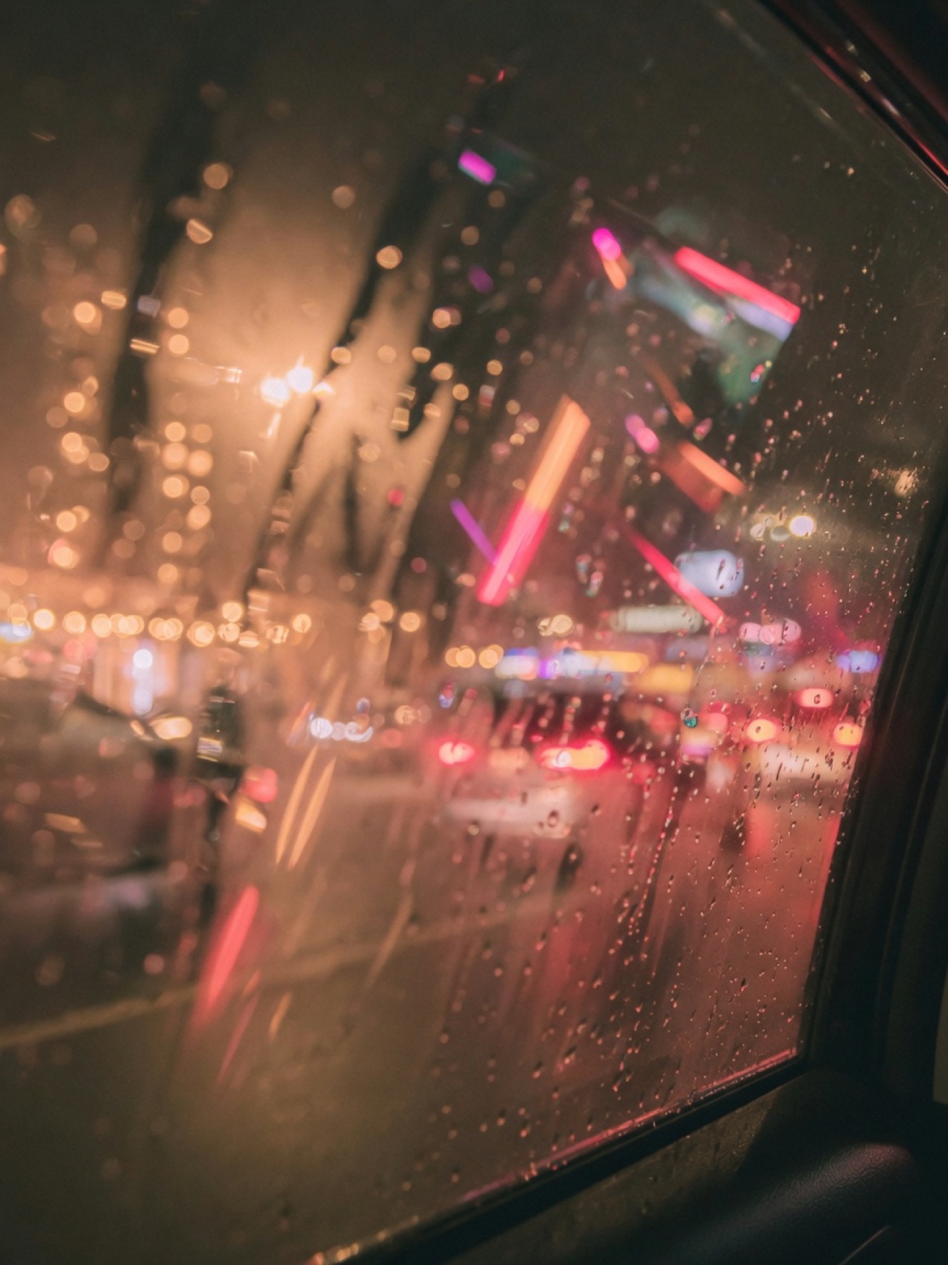 Rain on a car window at night with cherry and amber city lights