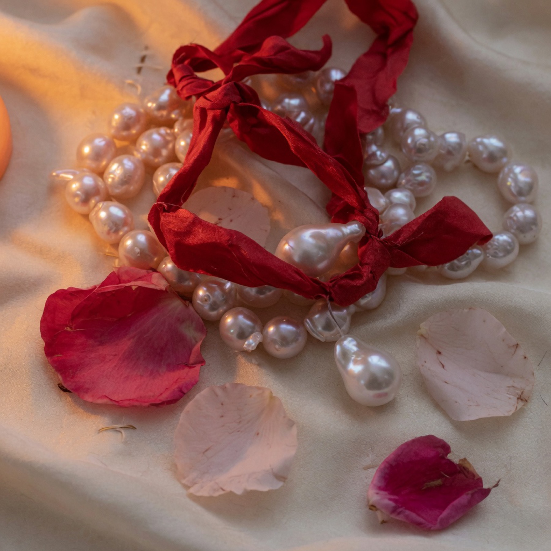 Baroque pearls tied with a crushed cherry silk ribbon among rose petals